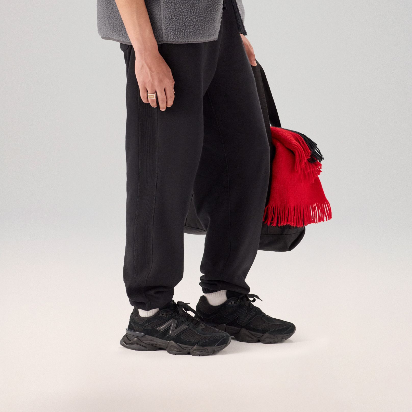 Jeune homme en pantalon noir et chaussures debout sur un fond gris.